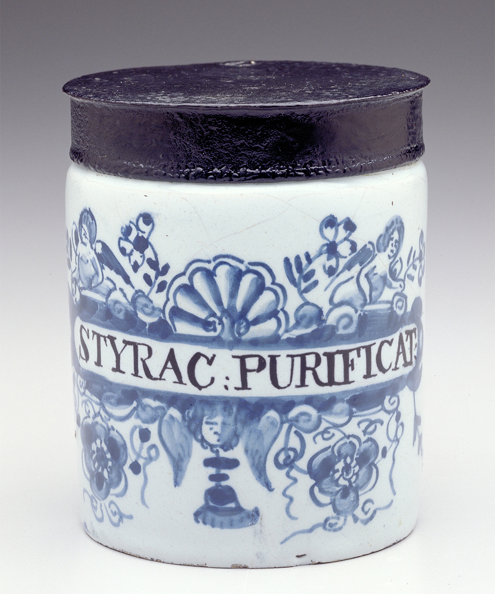 A small white ceramic drug pot with blue painted decoration and a metal lid.